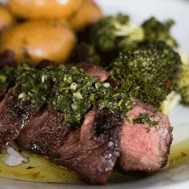 Sliced steak with green herb sauce and vegetables