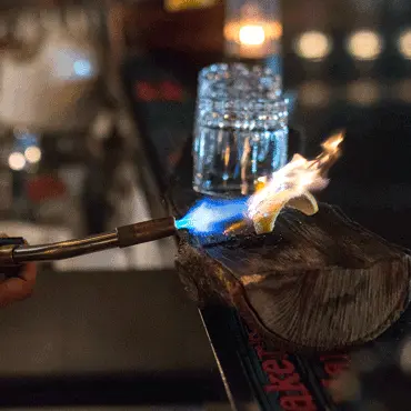 A flame toasting a garnish beside a cocktail glass