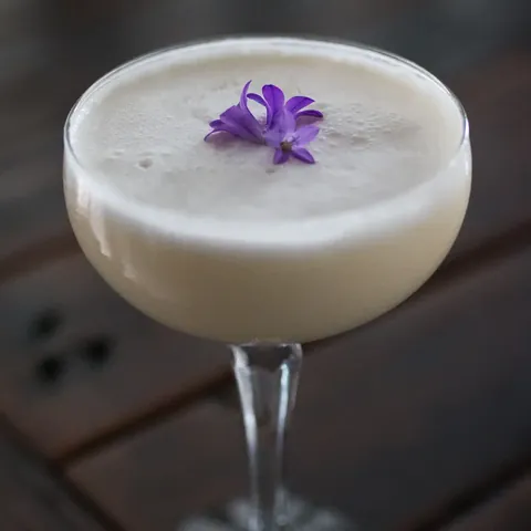 Foamy cocktail in a coupe glass topped with a purple flower