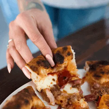 A hand lifting a slice of melted-cheese pizza